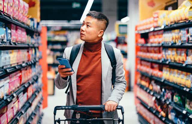 A man in a brown turtleneck sweater walks along a grocery aisle.