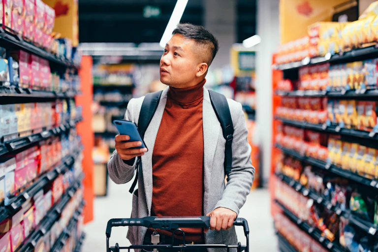 A man in a brown turtleneck sweater walks along a grocery aisle.