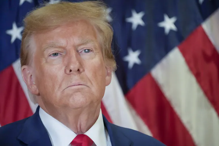 A man looks defiantly at the camera in front of an American flag
