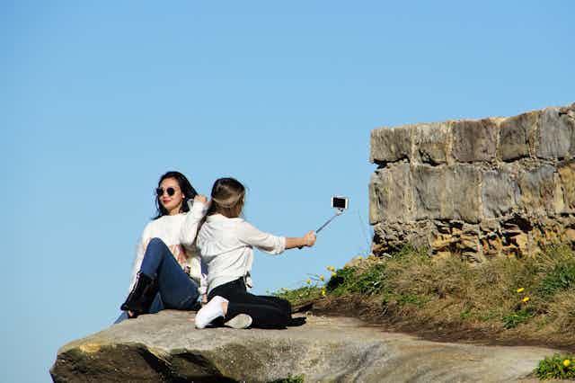 two women pose for selfies on cliff edge