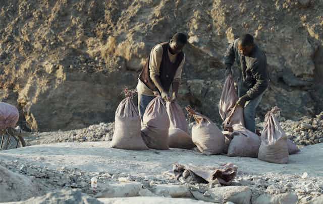 Two men load ore into sacks.