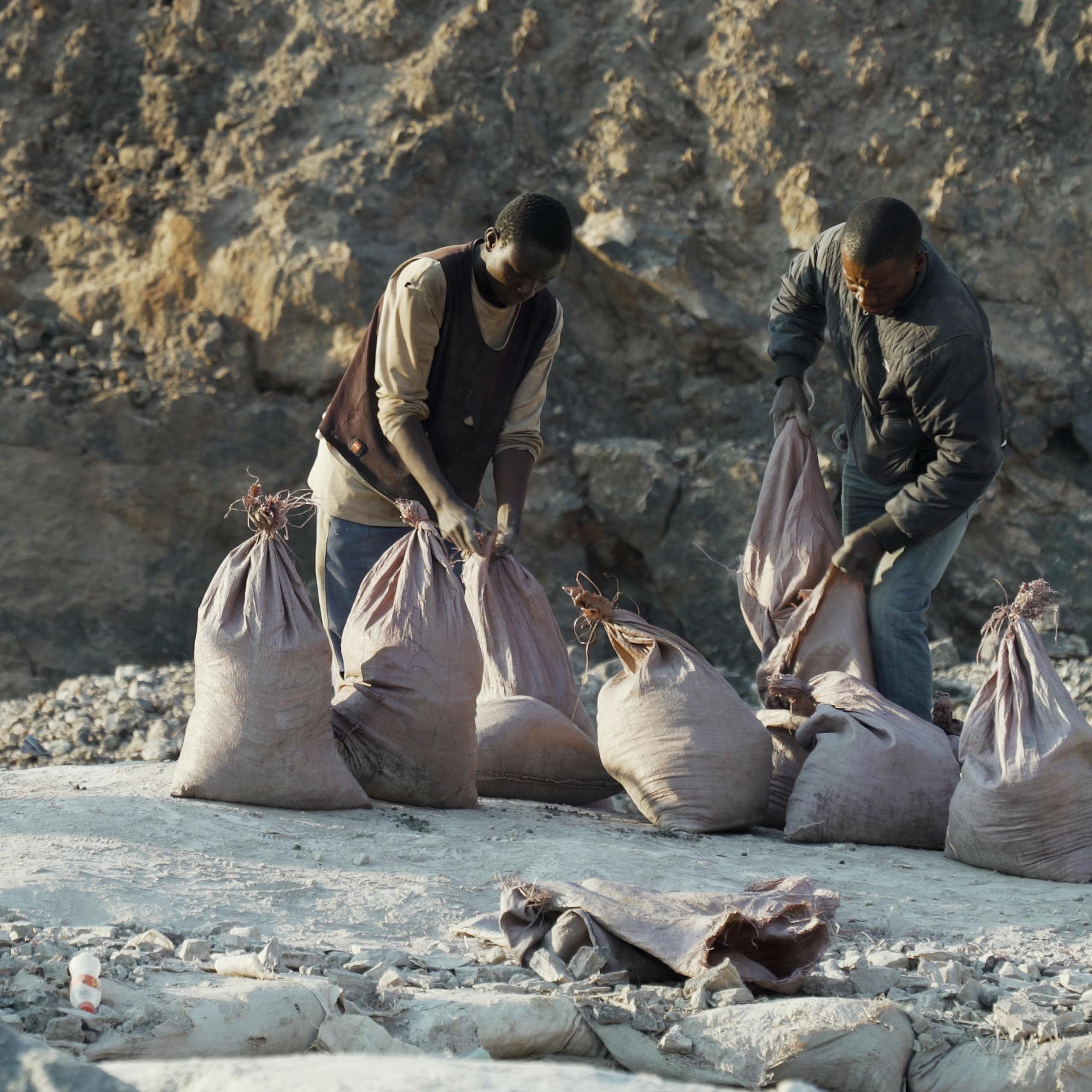 Two men load ore into sacks.