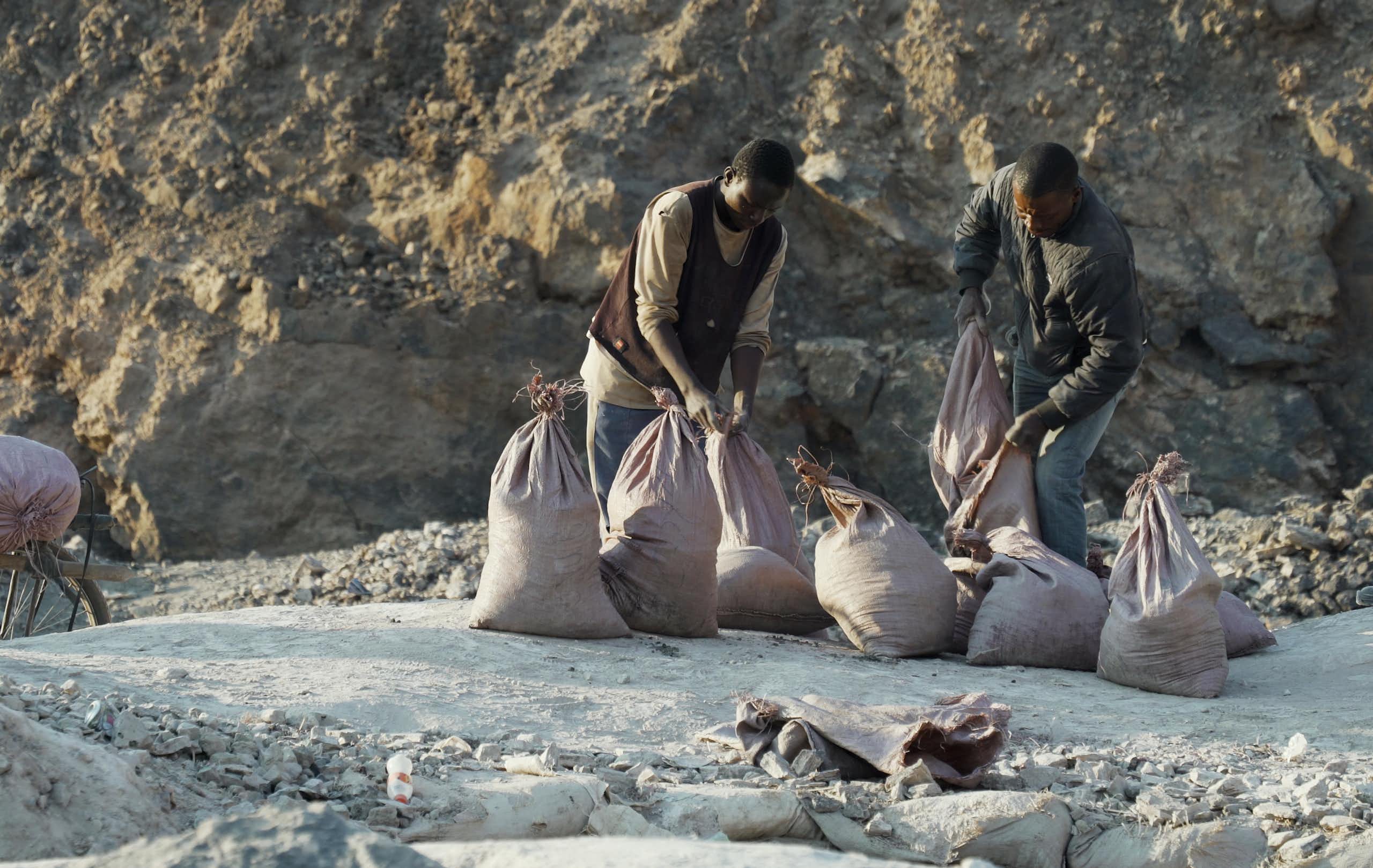 Two men load ore into sacks.