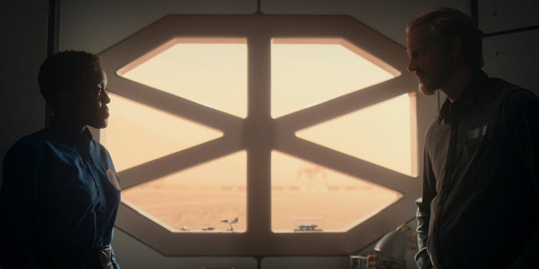 Two people on either side of an octogonal window.