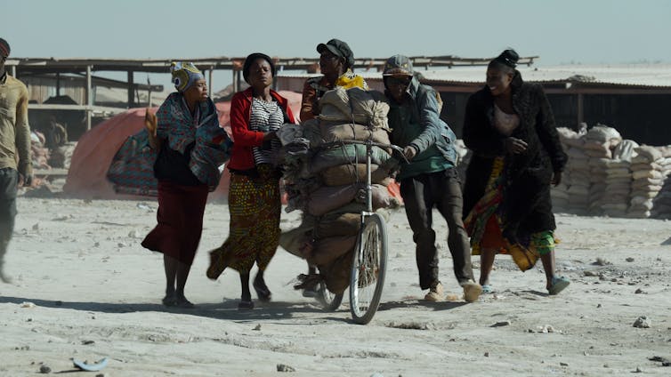 Two men hauling sacks of cobalt on a bike surrounded by three women.