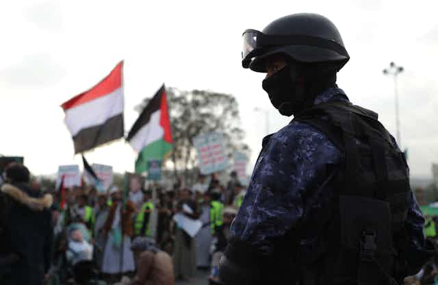 A man in military garb stands in front of protesters.