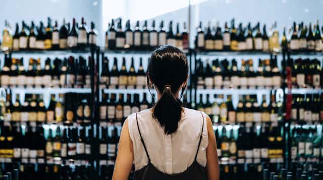A woman seen choosing between wines at a liquor store.