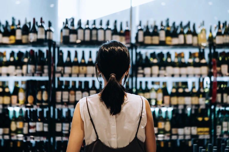A woman seen choosing between wines at a liquor store.