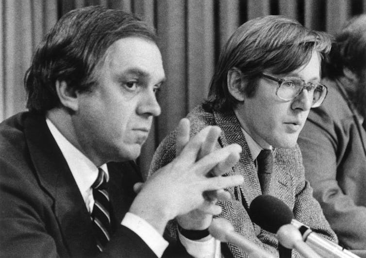 A black-and-white photo of two men in suits sitting at a table