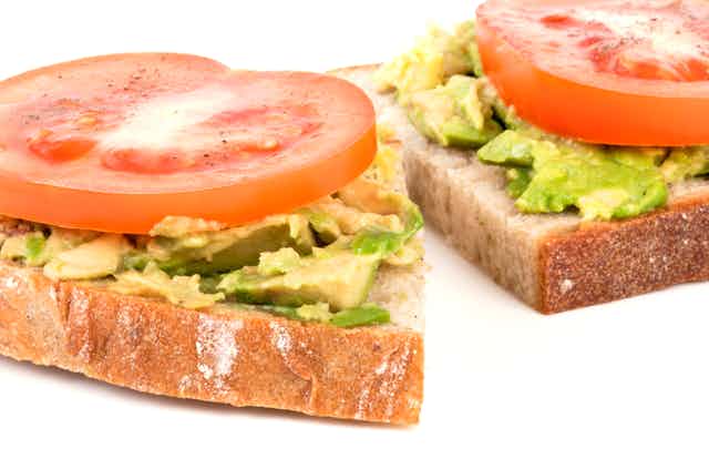 Close-up photograph of two pieces of toast with an avocado spread, topped with tomato slices.