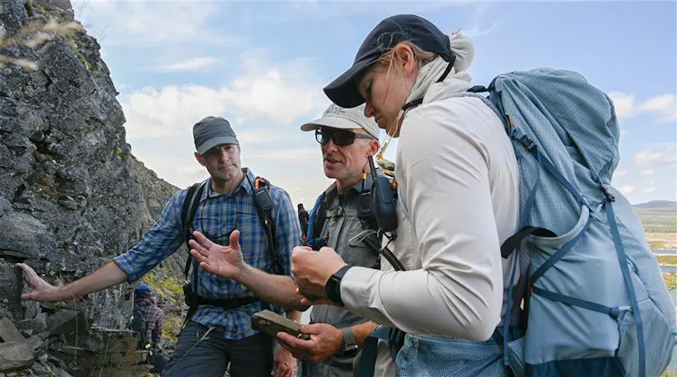 three people study a rock outcrop