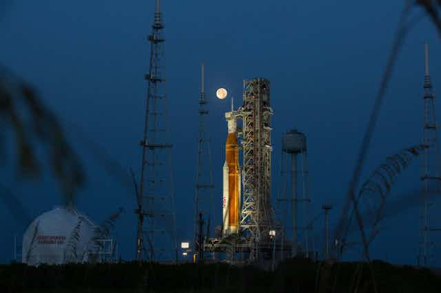 a rocket prepared for launch at night with the moon in the background