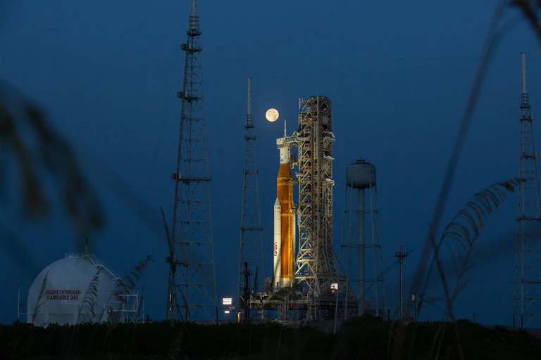 a rocket prepared for launch at night with the moon in the background
