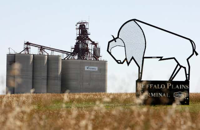 A wire sculpture of a buffalo with the words 'Buffalo Plain Terminal' sits in the foreground, while a grain elevator is seen in the background 