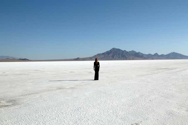Artist in a black dress standing on barren terrain in front of mountains