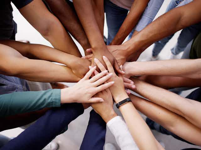 Close up of a group of people's hands piled on top of each other in the centre of a circle of people