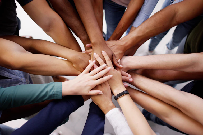 Close up of a group of people's hands piled on top of each other in the centre of a circle of people