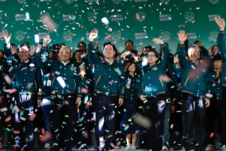 A large group of people in green jackets wave under falling confetti