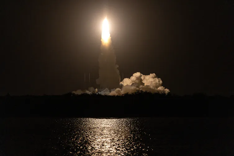 A rocket launching into the air over water at nighttime