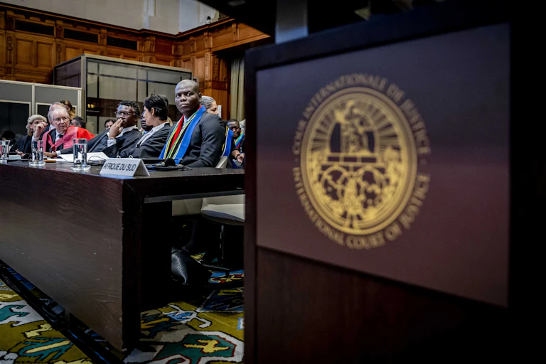 Some people in suits sit behind a desk to the left of an International Court of Justice sign