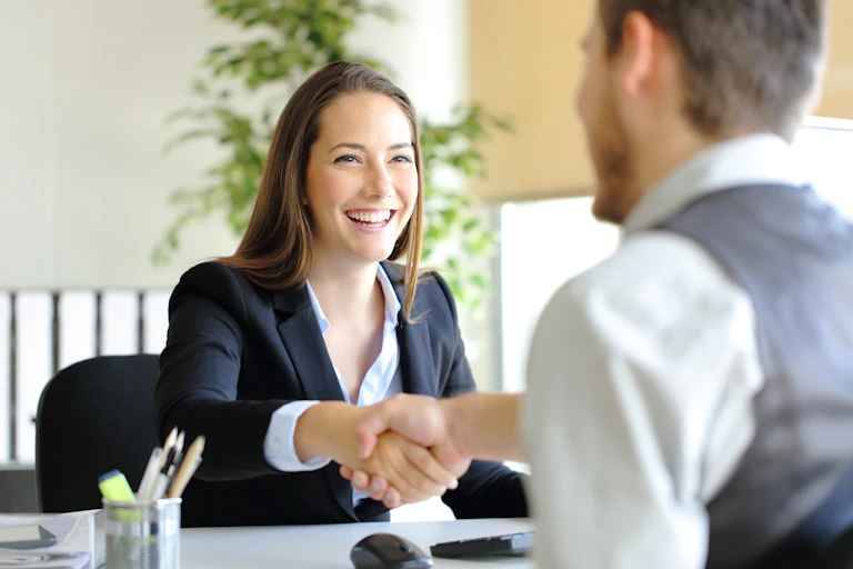 Woman behind desk shakes hand with man seated across from her