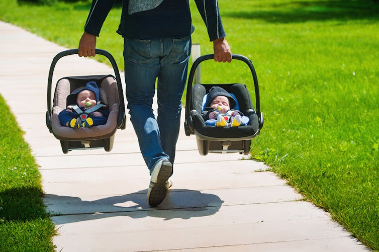 A person carrying two baby carriers with identical twin babies