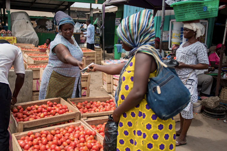 A woman sells tomatoes to a customer at her stand