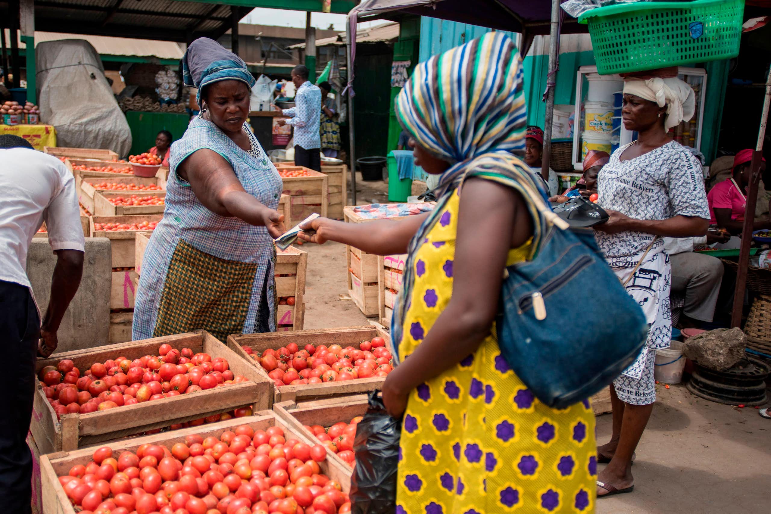 A woman sells tomatoes to a customer at her stand 