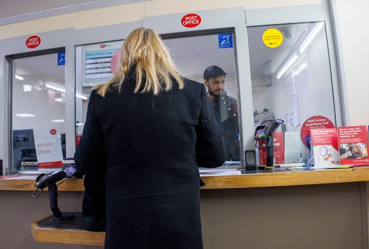 A woman standing at a Post Office counter.