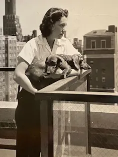 A sepia photo of a woman holding two sausage dogs.