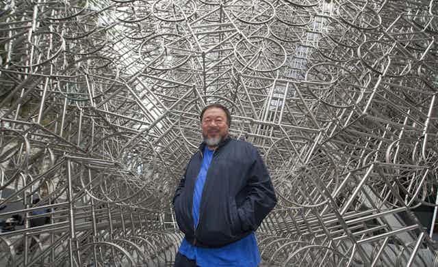 Ai Weiwei in front of a endless sculpture of bicycles. 