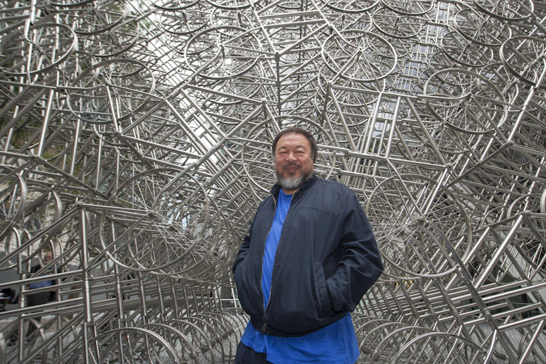 Ai Weiwei in front of a endless sculpture of bicycles.