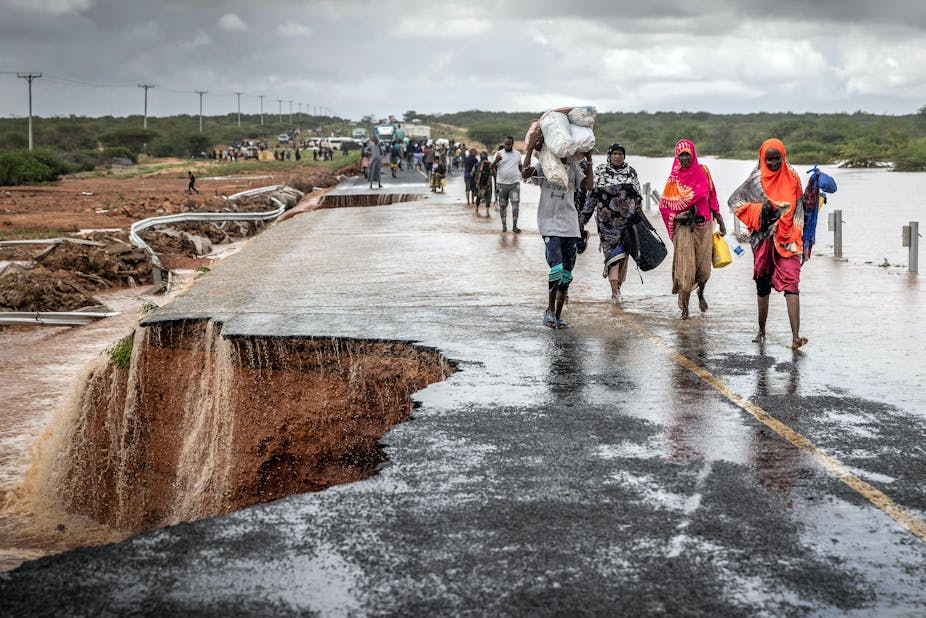 People carrying bundles walk past a collapsed section of road.