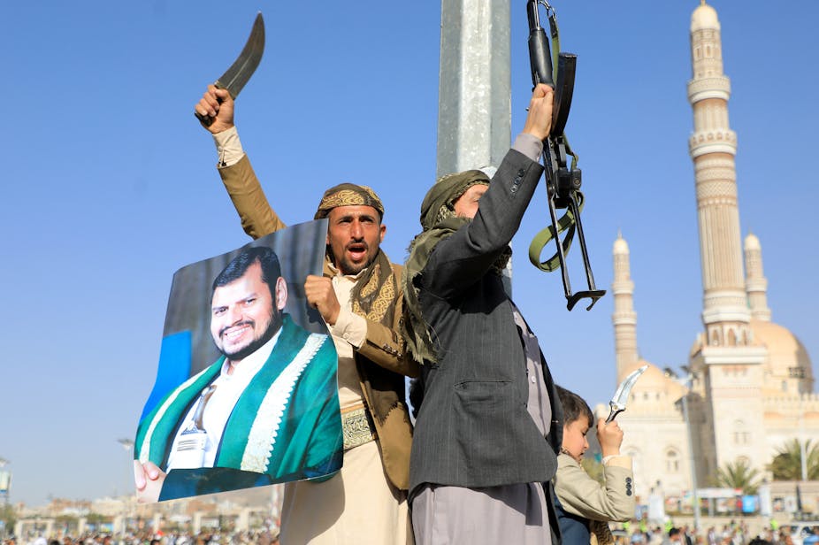 Deux hommes brandissent des armes et un portrait d'Hussein al-Houtji