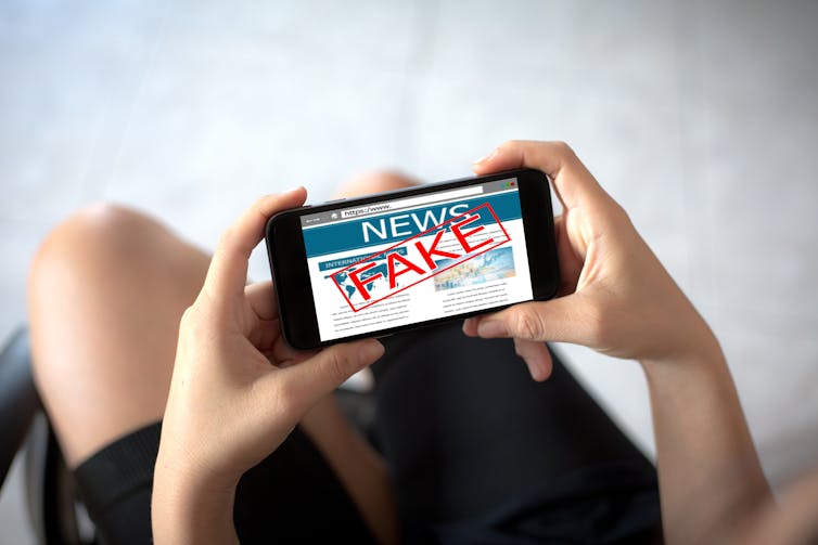 A phone showing the news with the word 'fake' written across it.