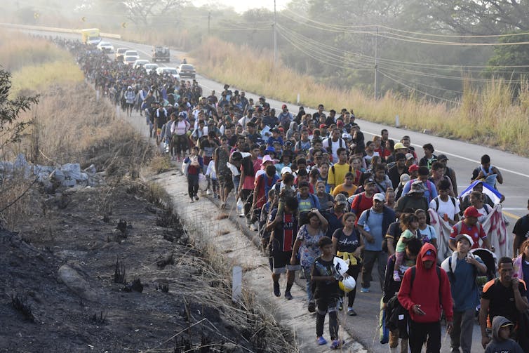 A long line of people walk along a dusty highway.