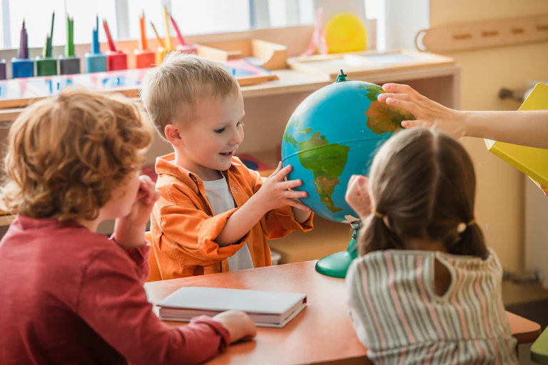 A bright-eyed little boy touches a globe as two other children watch on