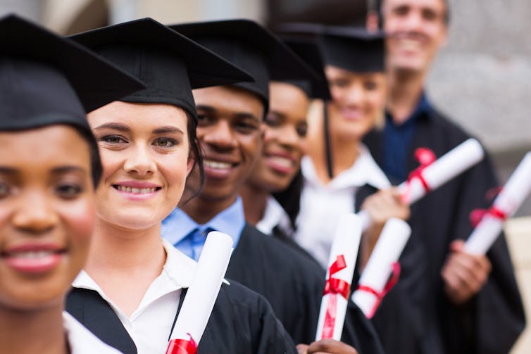 Group of graduates standing in a row wearing caps and gowns holding diplomas