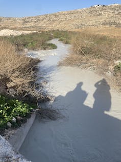 A polluted stream with cloudy white water with dry grassy hills surrounding it.