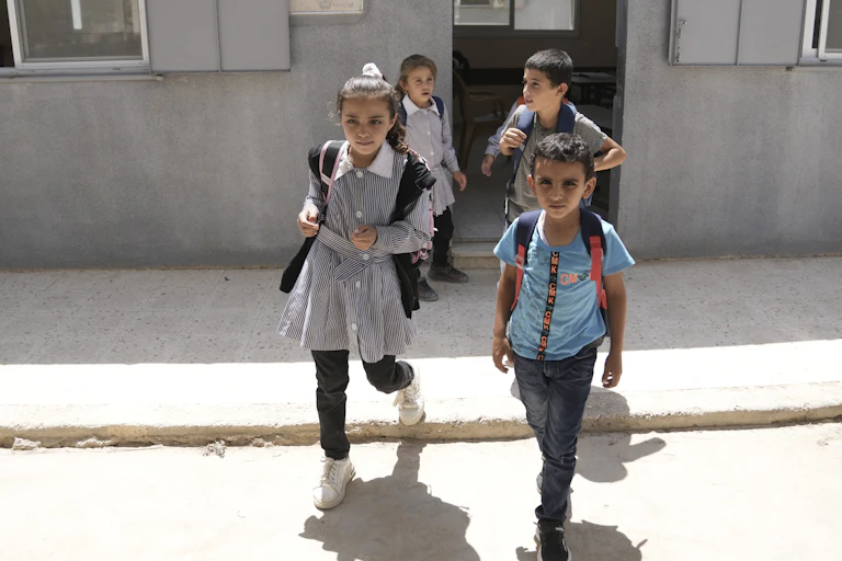 Young school children leave a school on a sunny day.