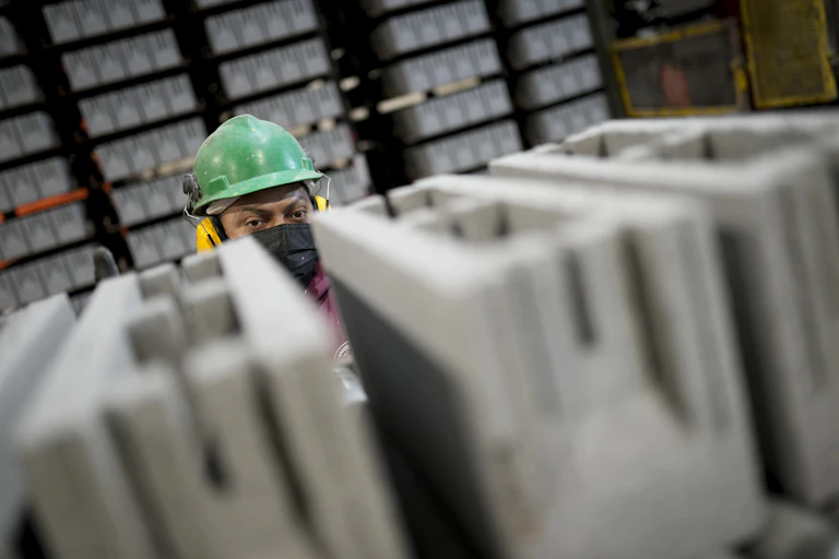A worker in hard had peers over the top of newly produced cement blocks