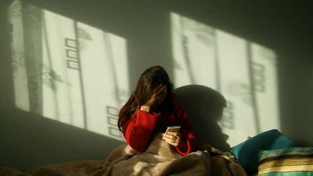 a girl holds her head in one hand while she's looking at a mobile phone while sitting in bed