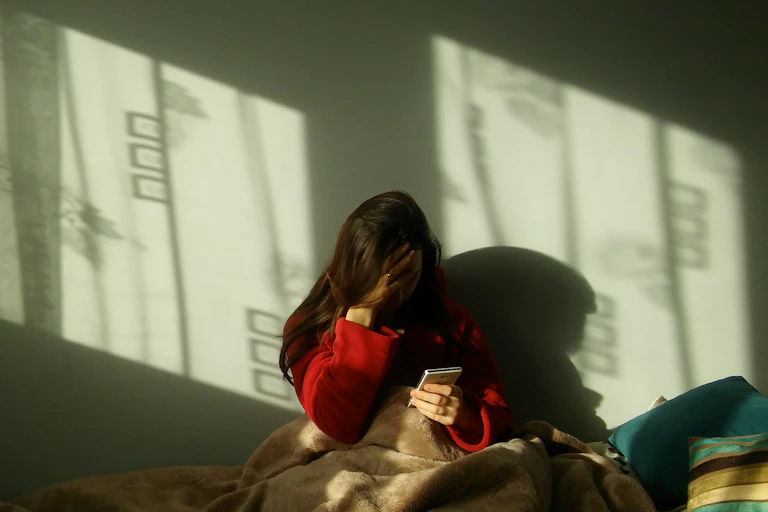 a girl holds her head in one hand while she's looking at a mobile phone while sitting in bed