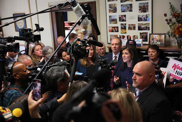 A dark haired woman surrounded by a pack of reporters.