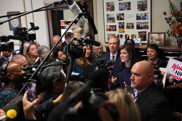 A dark haired woman surrounded by a pack of reporters.