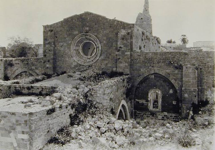 Ruins of an ancient monument that show a few intact walls, with stones and other debris scattered around.