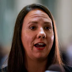 A woman with longer hair and light on her face speaks.