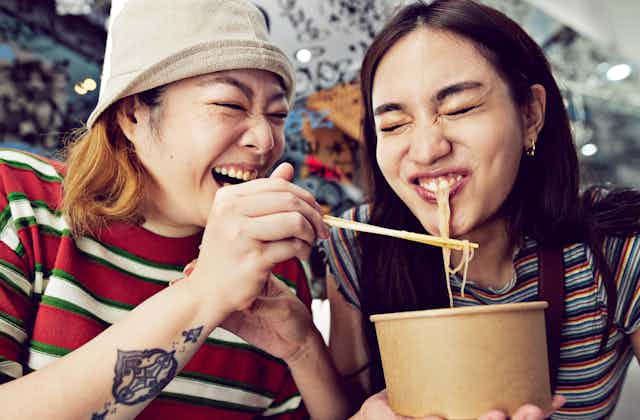 Woman with chopsticks feeds noodles to a friend.