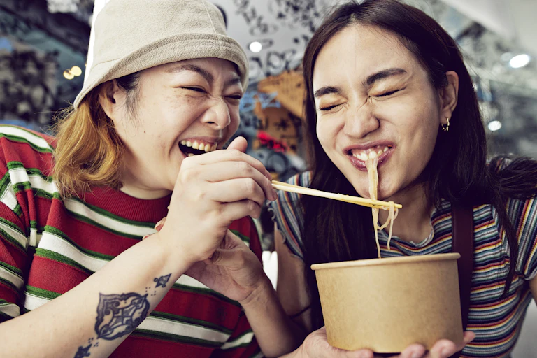Woman with chopsticks feeds noodles to a friend.