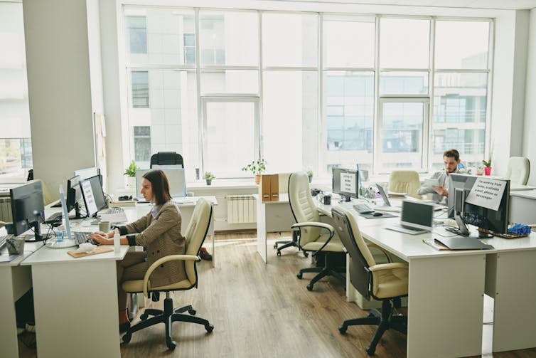 Two workers sit several desks away from each other in an otherwise empty office